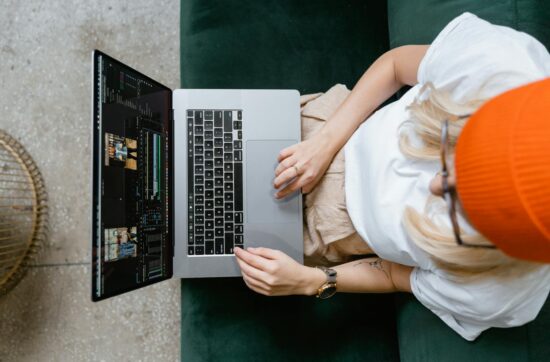 Top view of a woman editing video content on a laptop, wearing a casual outfit and orange beanie.
