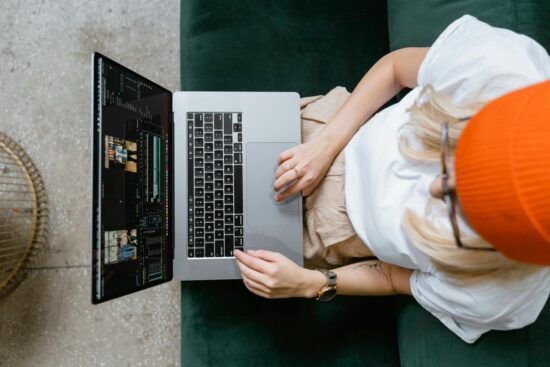 Top view of a woman editing video content on a laptop, wearing a casual outfit and orange beanie.