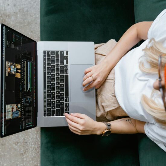 Top view of a woman editing video content on a laptop, wearing a casual outfit and orange beanie.