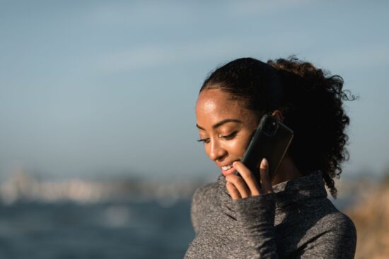 Young woman smiling during a phone call by the sea on a sunny day.