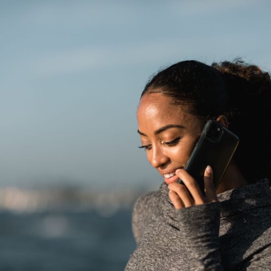 Young woman smiling during a phone call by the sea on a sunny day.